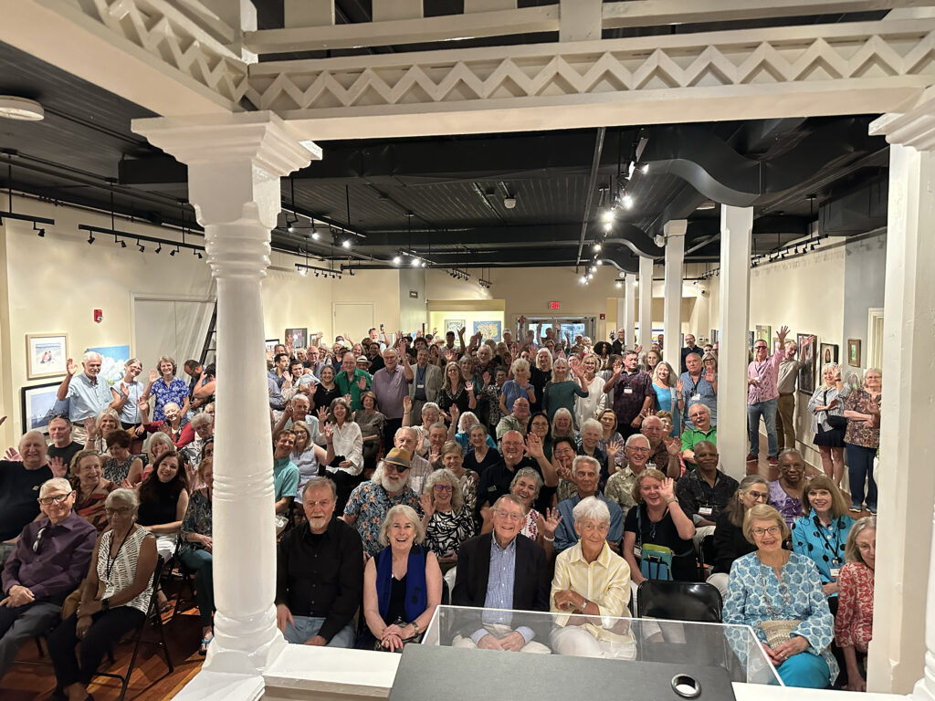 Large crowd of people smiling and waving inside an art gallery, gathered for the 37th annual Art in Gadsden event.