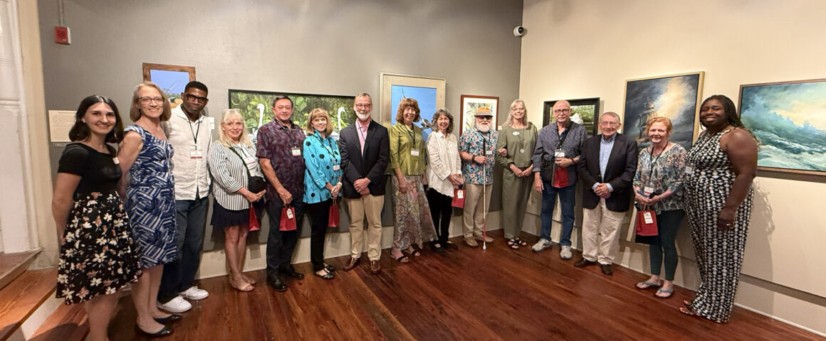 Group of adults posing for a photo in an art gallery, standing in front of paintings along the wall.