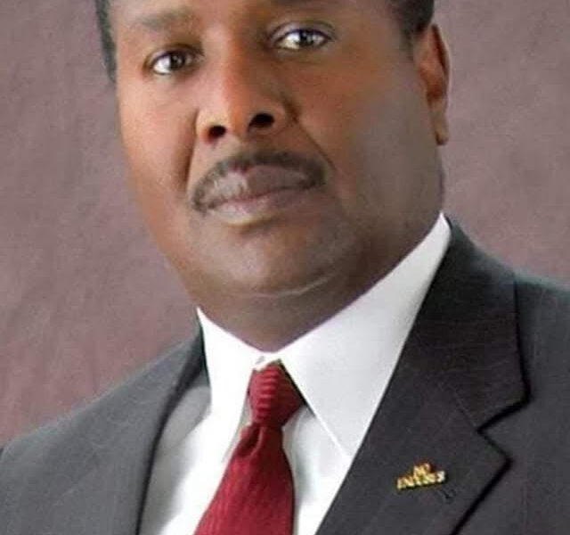 Formal portrait of Reginald James wearing a dark pinstripe suit, white shirt, and red tie, looking confidently at the camera with a neutral background.
