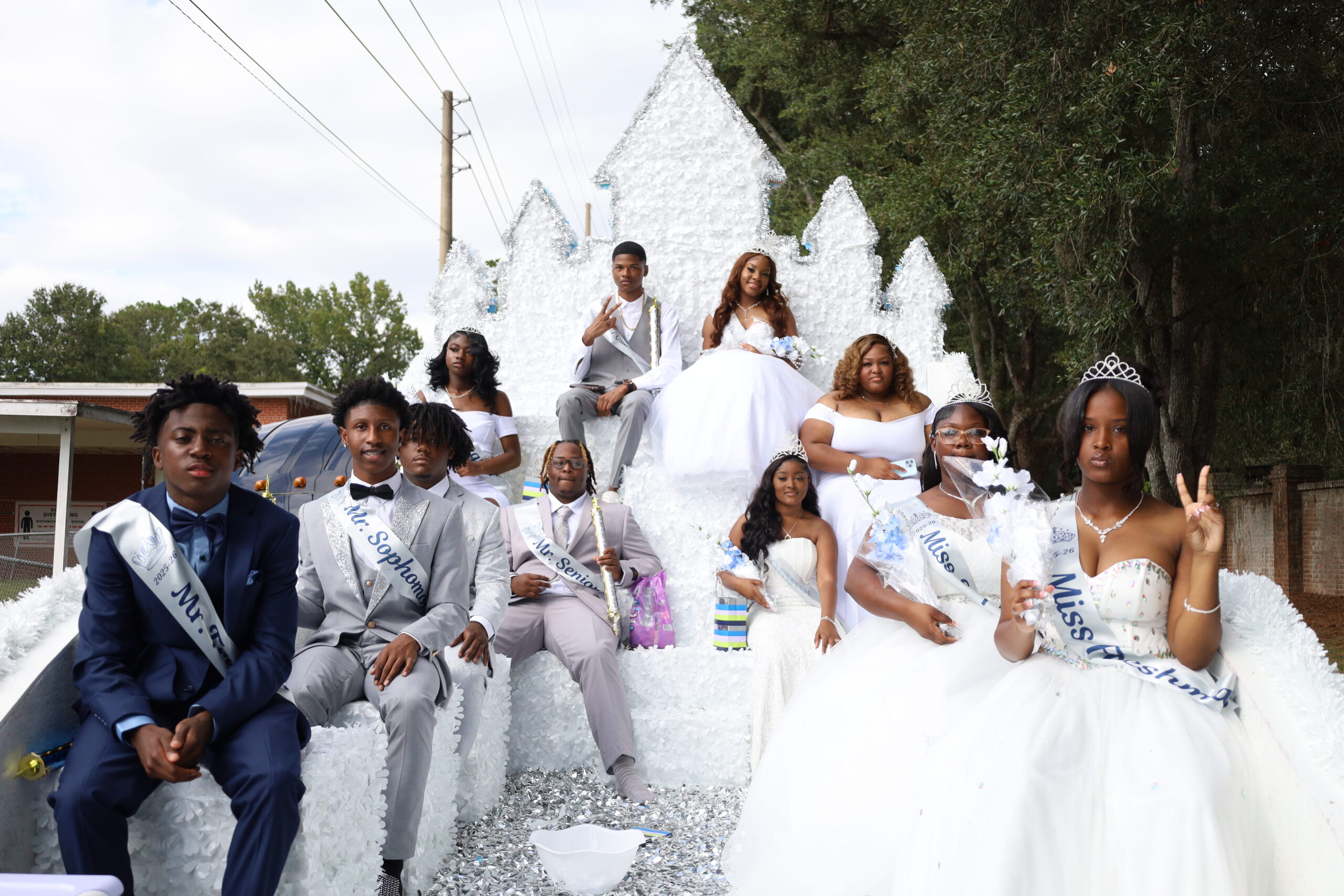 Homecoming court dressed in formal attire sits on a white parade float decorated like an ice castle, smiling for the camera.