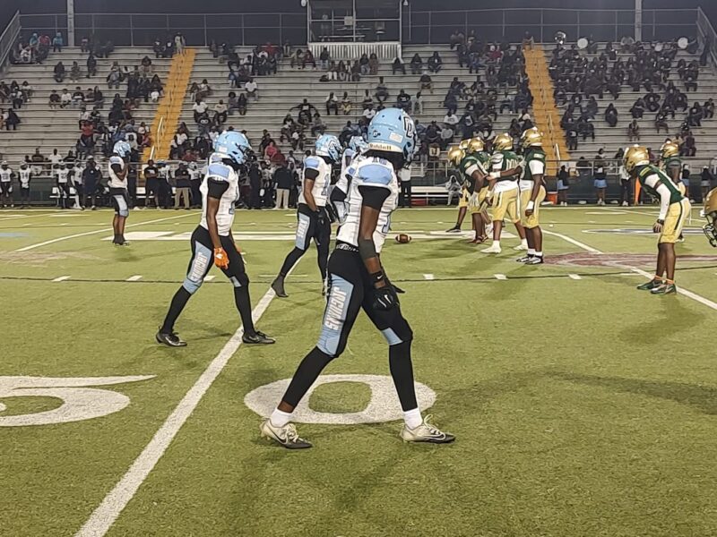 Football teams line up at the 50-yard line under stadium lights during a night game.