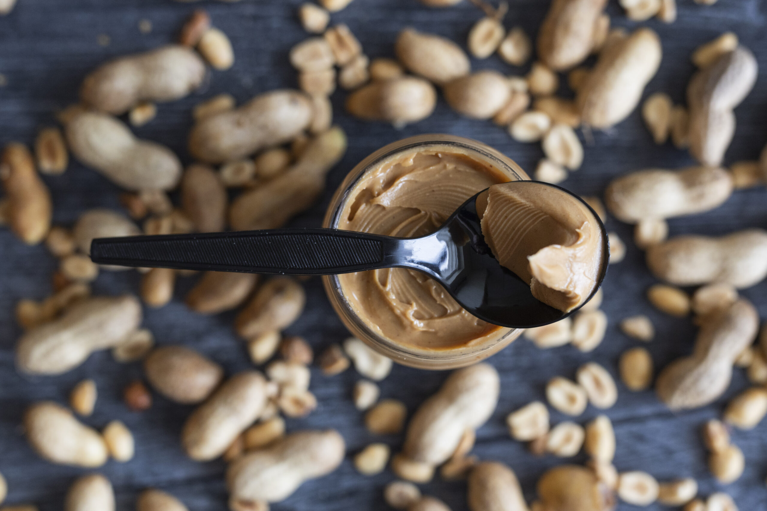 Spoon resting on a jar of peanut butter surrounded by peanuts.
