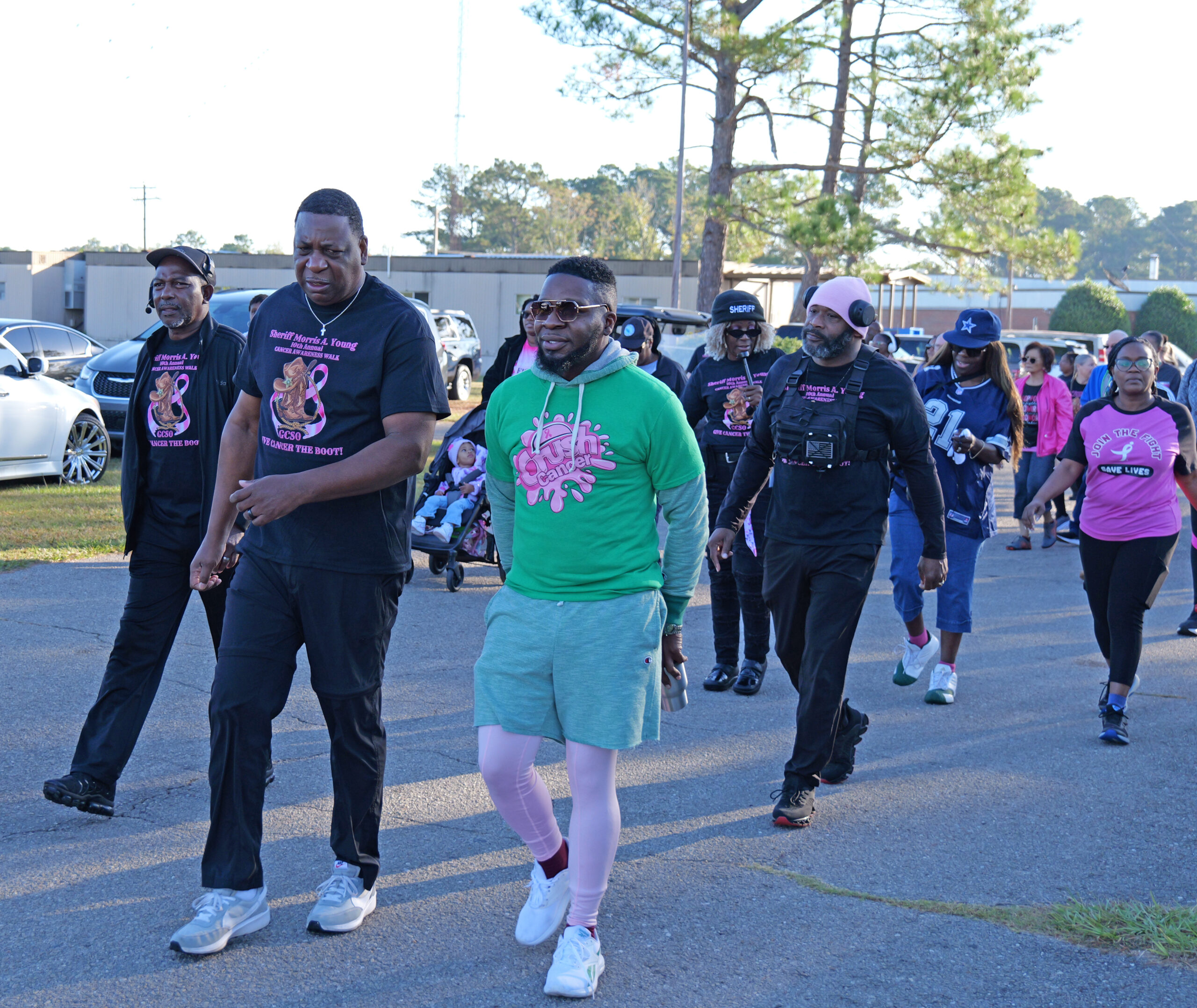 Large group of participants wearing pink and black shirts walking together outdoors for a breast cancer awareness event.
