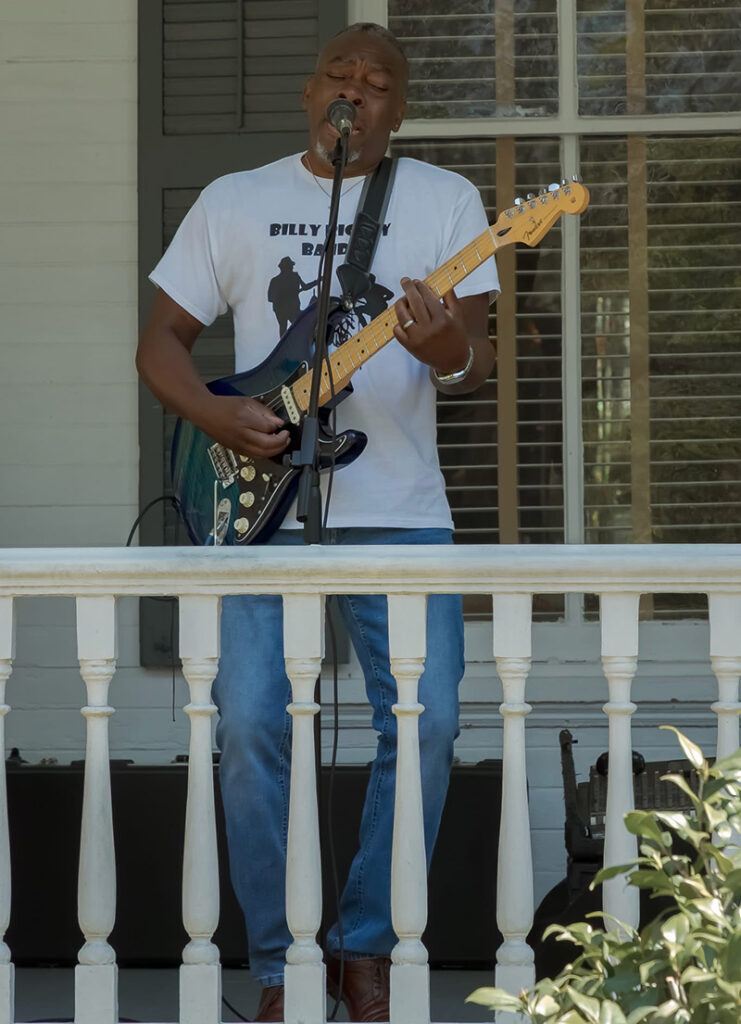 Musician Billy Rigsby singing and playing electric guitar while performing on a porch stage during Quincy Porchfest.