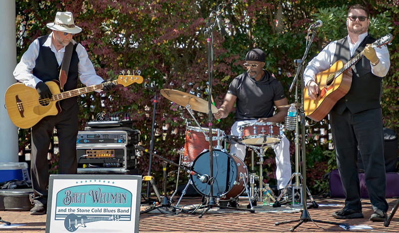 Brett Wellman and the Stone Cold Blues Band performing live outdoors with bass, drums, and acoustic guitar during Quincy Porchfest.