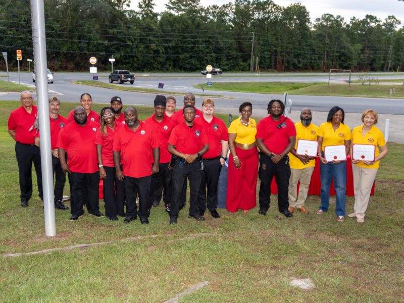 A large group pose of city staff, officials, and committee members wearing red and yellow shirts standing outdoors.