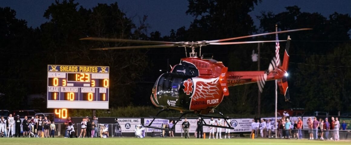 A red Survival Flight medical helicopter hovering above a football field next to a scoreboard showing the Sneads Pirates.